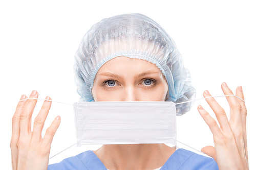 Portrait of attractive young surgeon with blue eyes putting face mask while preparing for operation