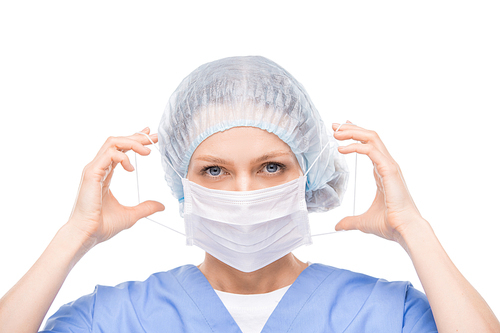 Contemporary young doctor, dentist or surgeon putting on protective mask on her face before operation or medical procedure