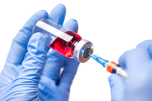 Close-up of unrecognizable doctor in blue gloves filling syringe with red liquid medication against white background