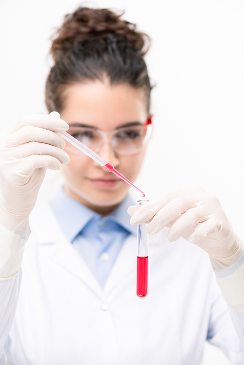Young clinician or chemist in protective eyeglasses, gloves and whitecoat adding red fluid into flask with new vaccine
