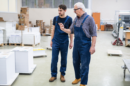 Serious white-haired man in glasses gesturing hand while explaining task to printing house worker