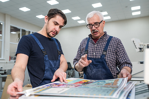 Experienced senior worker in glasses explaining young man how to estimate print quality during his internship
