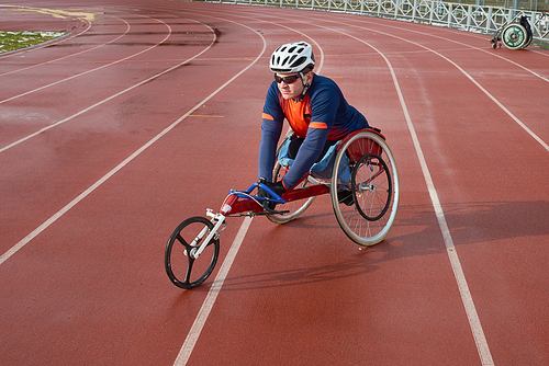 Handicapped sportsman in helmet and sunglasses sitting in racing wheelchair at outdoor track and field stadium and getting ready for marathon