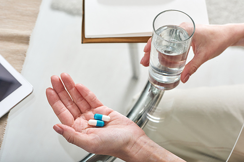 Above view of unrecognizable woman sitting at glassy table and taking medication