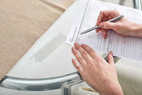 Hands of young female social worker with pen over paper helping her client with filling in health insurance claim form