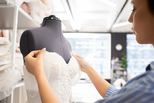 Professional seamstress working on wedding dress corset in bridal workshop, horizontal shot