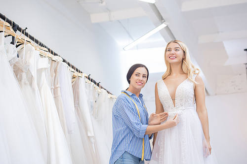 Friendly wedding designer working with young bride at gown fitting in store