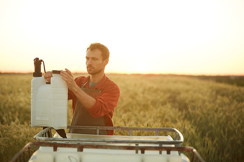 Portrait of male worker holding spraying can while standing by water tank in field at sunset, copy space