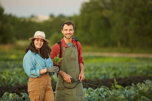 Portrait of two workers in field at vegetable plantation, young woman and man smiling at camera in foreground, copy space