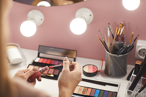 Close up of unrecognizable young woman opening lip gloss while doing make up at dressing table, copy space