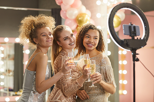 Multi-ethnic group of beautiful young women holding champagne glasses and smiling while posing for camera in dressing room