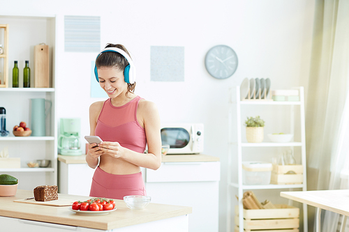 Waist up portrait of smiling young woman listening to music while preparing fitness lunch in kitchen interior, copy space