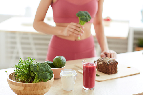 Close up of unrecognizable young woman preparing fitness lunch in kitchen, broccoli and smoothie shake in foreground, copy space