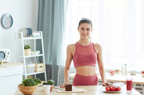 Waist up portrait of fit young woman cooking healthy food in kitchen interior and smiling at camera, copy space