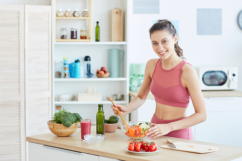 Waist up portrait of fit young woman cooking fitness food in kitchen interior and smiling at camera, copy space