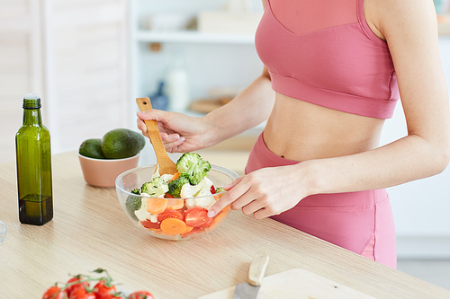 Close up of unrecognizable sportive woman stirring salad in bowl while cooking healthy food, copy space