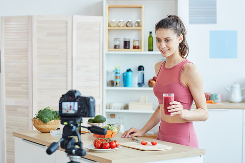 Waist up portrait of fit young woman recording cooking video while standing in kitchen interior, copy space