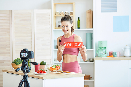 Waist up portrait of fit young woman holding FOLLOW sign while recording cooking video on healthy food, copy space
