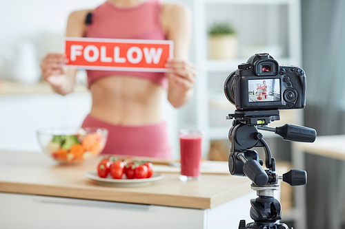 Blurred portrait of unrecognizable young woman holding FOLLOW sign while recording food video, focus on camera screen, copy space