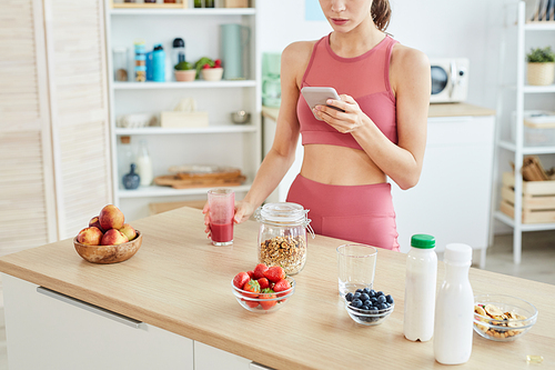 Cropped portrait of fit young woman using smartphone while cooking healthy snack in kitchen, copy space