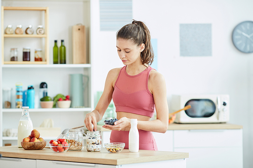 Waist up portrait of fit young woman making healthy granola snack in kitchen interior, copy space