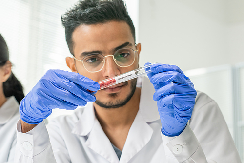 Gloved male worker of food quality control looking at several tiny pieces of raw vegetable meat in flask during scientific research in laboratory