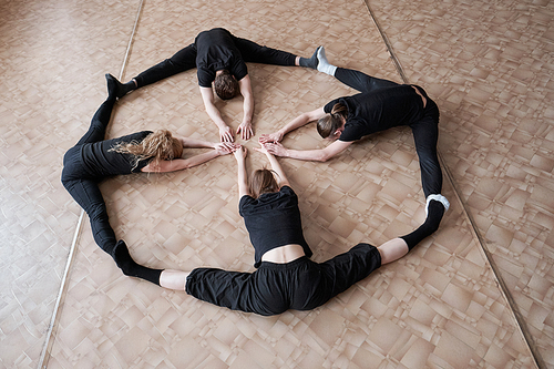 Horizontal high angle shot of unrecognizable dancers wearing black clothes doing stretching exercise on floor