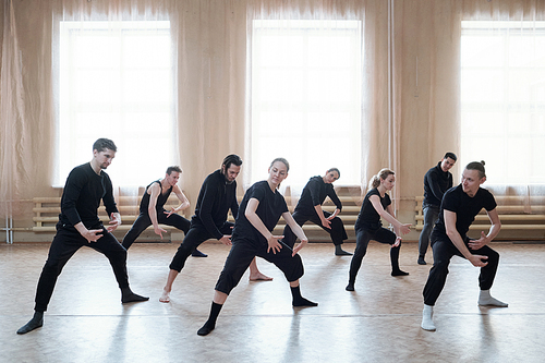 Horizontal shot of young men and women wearing black outfits dancing together in rehearsal studio room