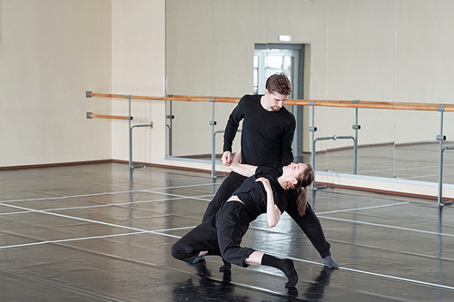 Young couple in black pants and t-shirts training one of dance exercise during lesson in large modern studio of dancing