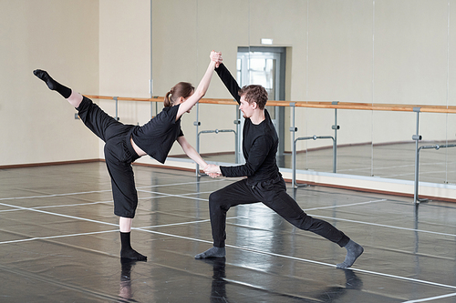Young man and woman in black rehearsing contemporary partner dance in studio, horizontal shot