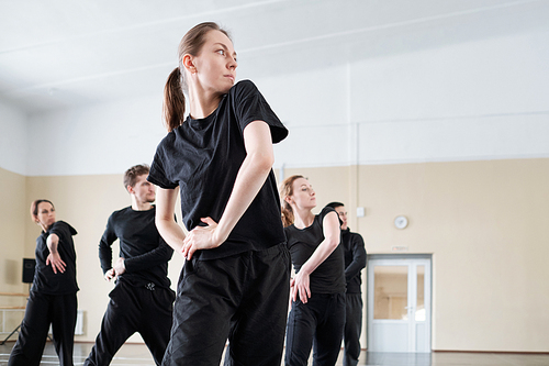 Group of young people in black outfits dancing together in rehearsal studio, horizontal low angle shot