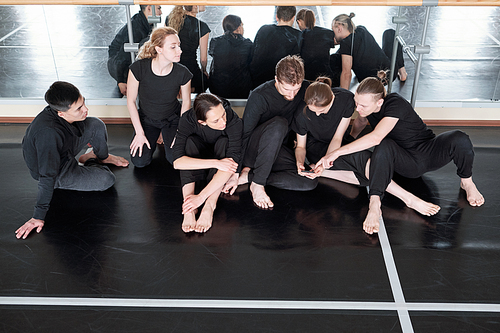 Contemporary dance teammates sitting together on floor against mirrors discussing something during break, high angle shot
