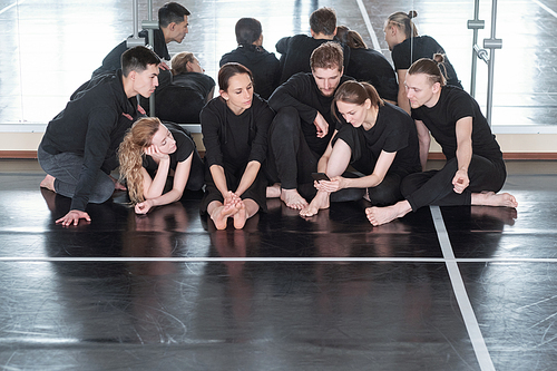 large group of young students of modern dance dancing course sitting on the floor by mirror while one of girls scrolling in smartphone