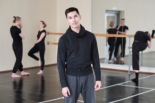 Horizontal medium long portrait of young man wearing black and grey outfit standing in rehearsal studio