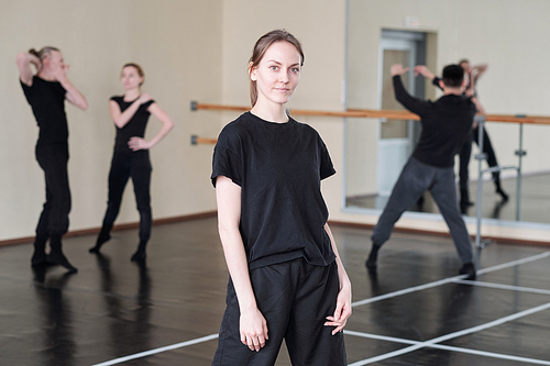 Horizontal medium long portrait of young woman wearing stylish black outfit standing in rehearsal studio