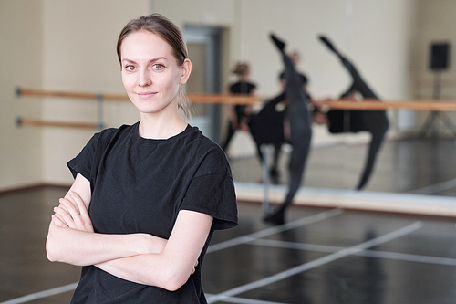 Horizontal medium portrait of young woman wearing black T-shirt standing with arms crossed in rehearsal studio