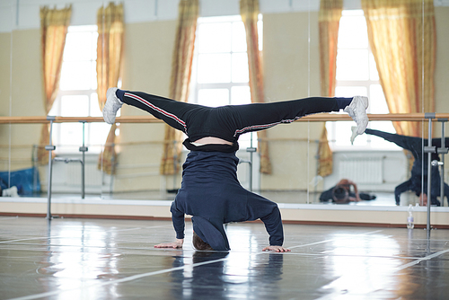 Horizontal shot of unrecognizable young man doing headstand in dance rehearsal studio room