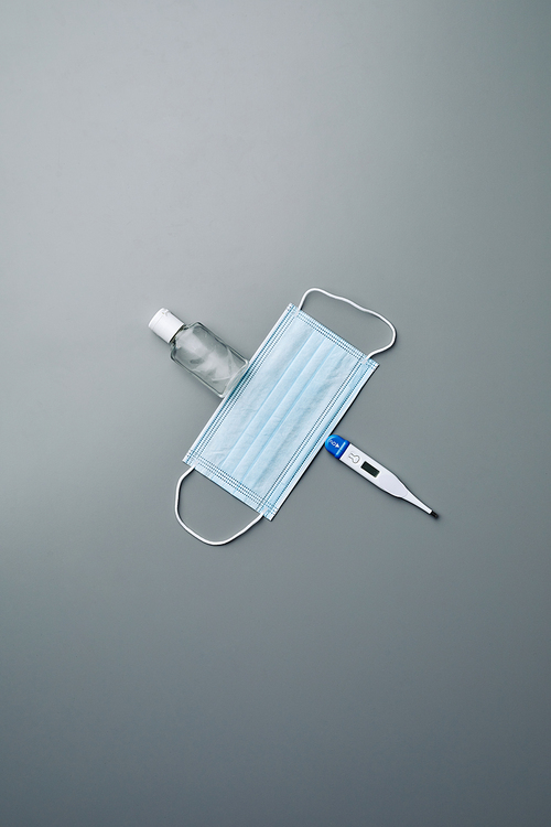 Minimal background composition of medical mask, hand sanitizer and thermometer laid over grey background, copy space
