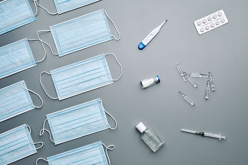 Top view background composition of medical masks, antibiotics and thermometer in laid out over grey background, copy space