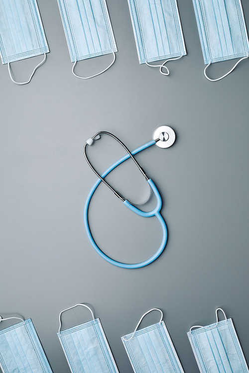 Above view background composition of medical masks framing stethoscope in center over grey background, copy space