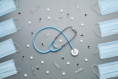 Above view composition of medical masks framing stethoscope and antibiotics laid out in pattern over grey background, copy space