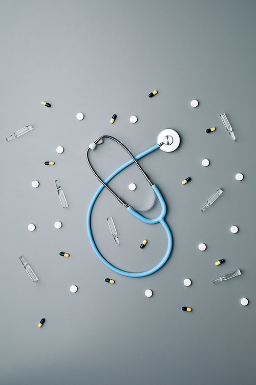 Above view medical background composition of stethoscope and antibiotics laid out in pattern over grey, copy space