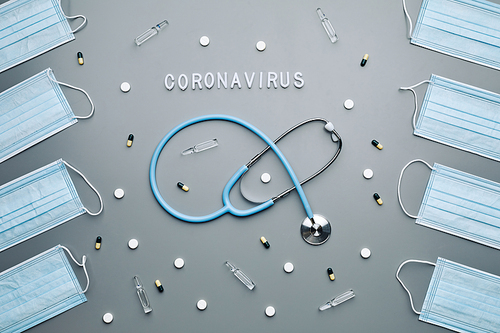 Above view composition of medical masks framing stethoscope and coronavirus medication laid out over grey background, copy space