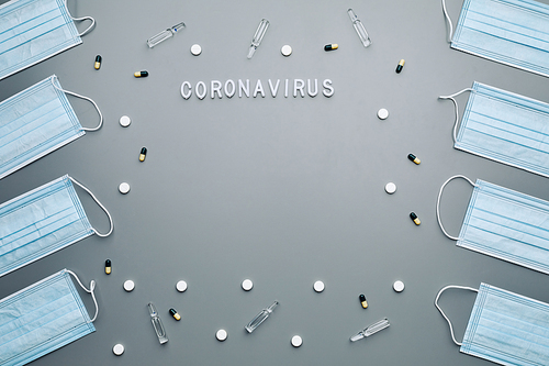 Above view composition of medical masks framing coronavirus word and medication laid out over grey background, copy space