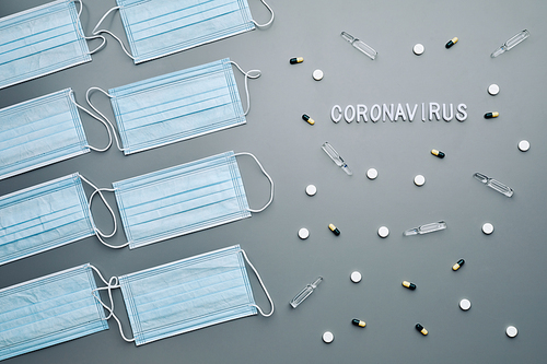 Above view composition of medical masks with coronavirus word and medication laid out in pattern over grey background, copy space
