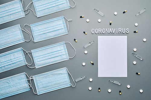 Above view composition of medical masks with coronavirus word and blank white paper laid out over grey background, copy space