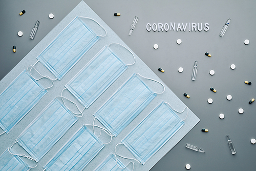 Top view composition of medical masks with coronavirus word and medication laid out in pattern over grey background, copy space