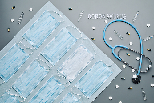Top down composition of medical masks with coronavirus word and sthetoscope laid out over grey background, copy space