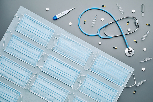 Top down composition of medical masks with stethoscope and medications laid out over grey background, copy space