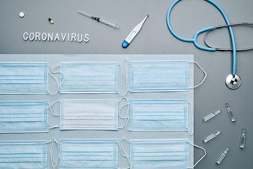 Minimal graphic composition of medical masks with stethoscope and coronavirus word laid out over grey background, copy space